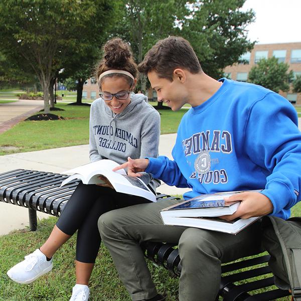 two college students sitting on a bench while looking at a textbook on the Blackwood campus